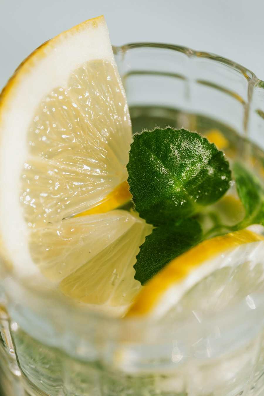 Close-up of fresh lemon wedges and mint leaves in infused water glass for natural hydration
